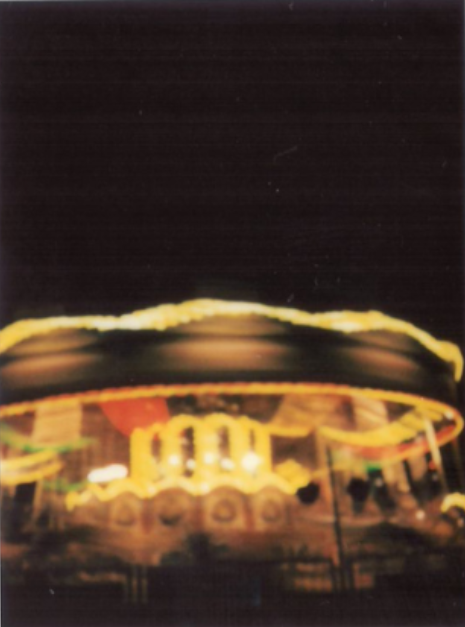 A carousel at night, its lights smeared into long golden streaks