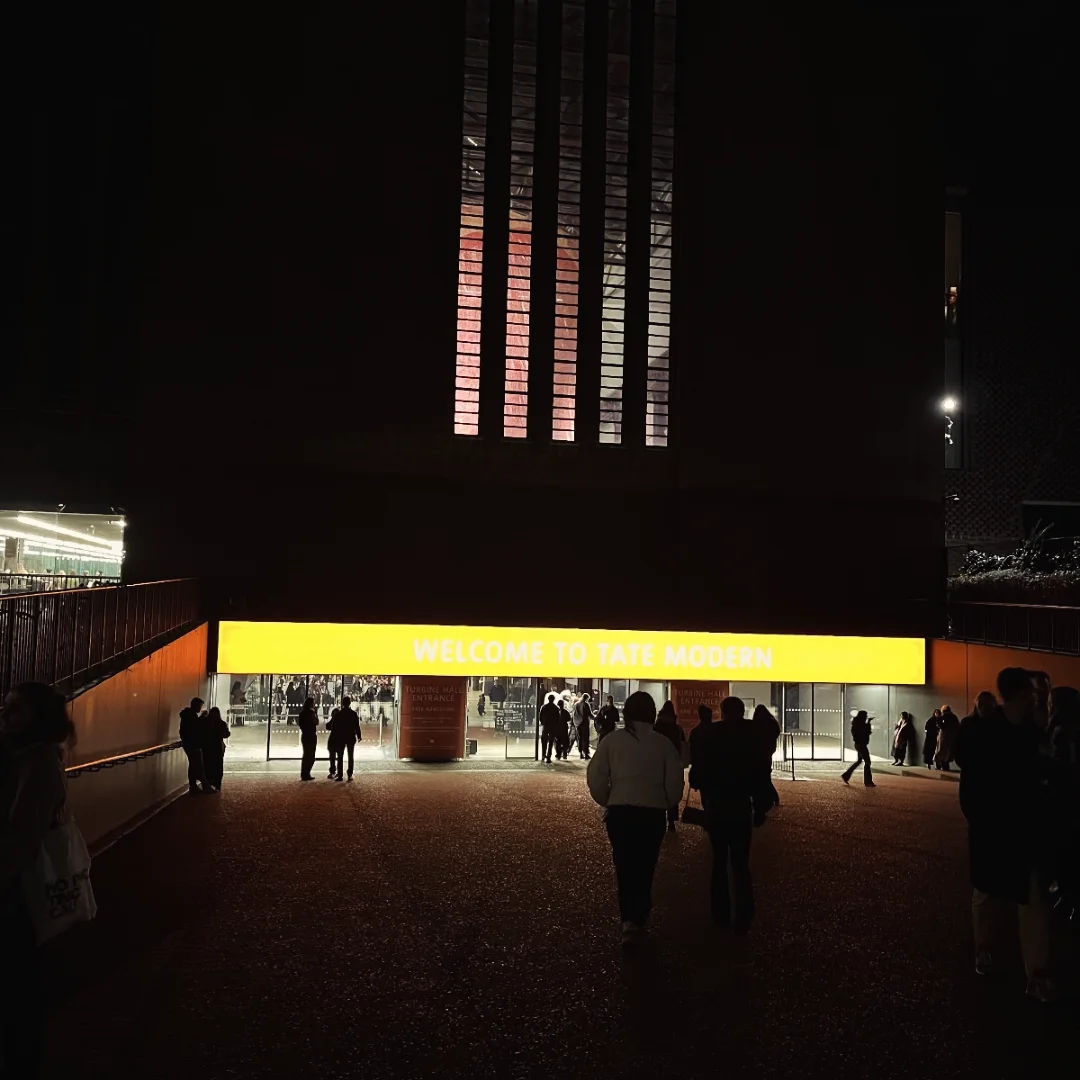 The Tate Modern entrance at night, its yellow welcome banner glowing against the dark